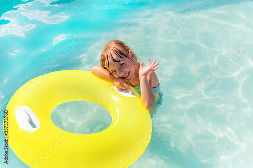 A little girl in the pool, on a Sunny day, swimming with tubing, waving her hand . An emotional portrait of a child, a pleasant time on vacation.
