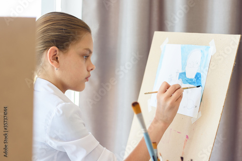 A girl in light clothes sits in front of an easel and draws still life