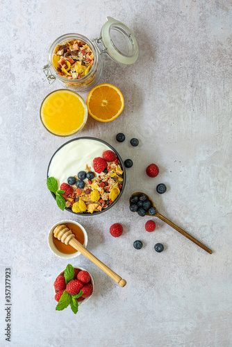 Vertical orientation. Healthy breakfast concept. Muesli, berries, honey, and fresh-squeezed orange juice. Top view, copy space