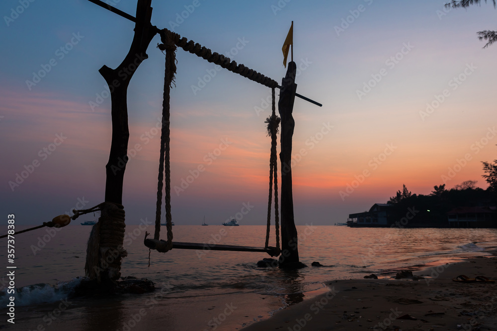 Silhouette wooden swing and calm sea, Tropical beach sunrise