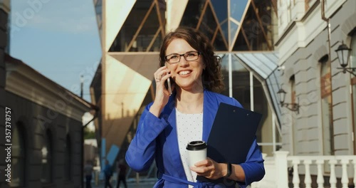 Successful businesswoman walking in city, talking by phone. Confident lady