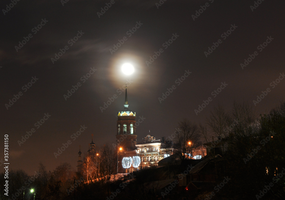 Night winter panorama of the city of Kungur. Full moon over the bell tower of the Orthodox Tikhvin temple.