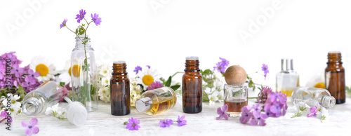 bottles of essential oil and colorful petals of flowers on white table in panoramic size