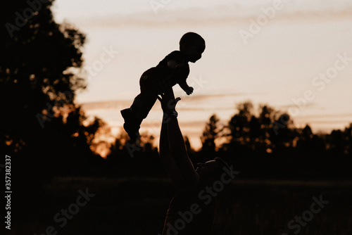 Fototapeta Naklejka Na Ścianę i Meble -  silhouette dad plays and throws his little son in the field in the summer