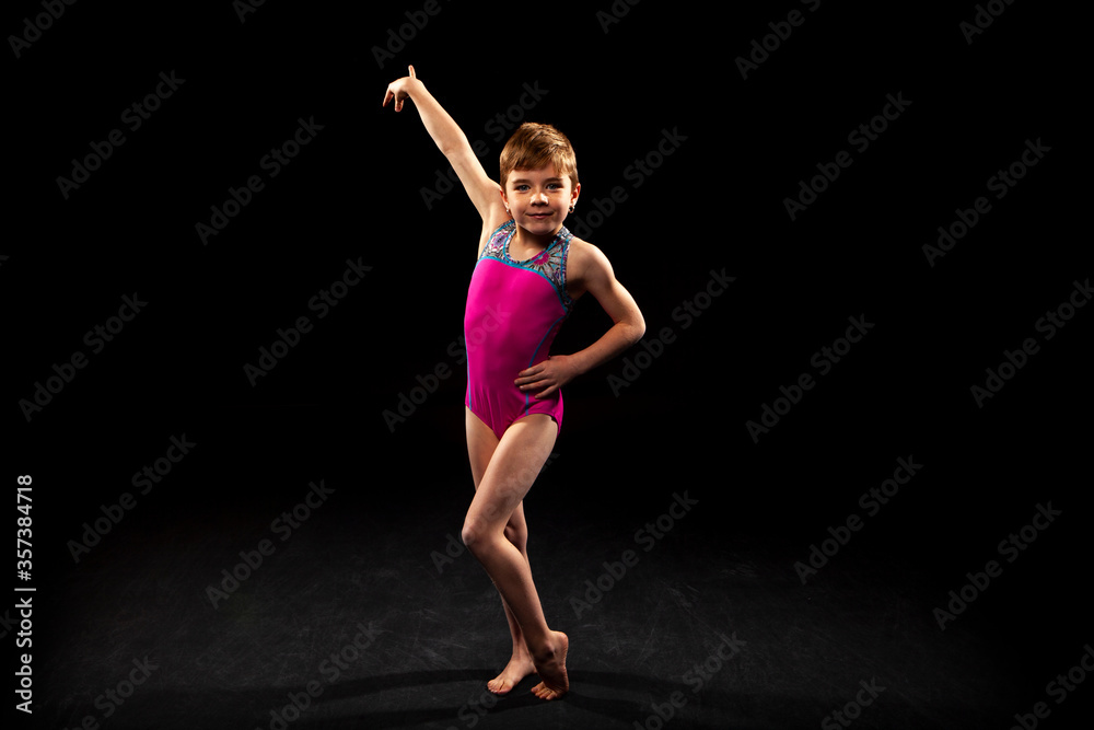 Young gymnast posing on a black background. 