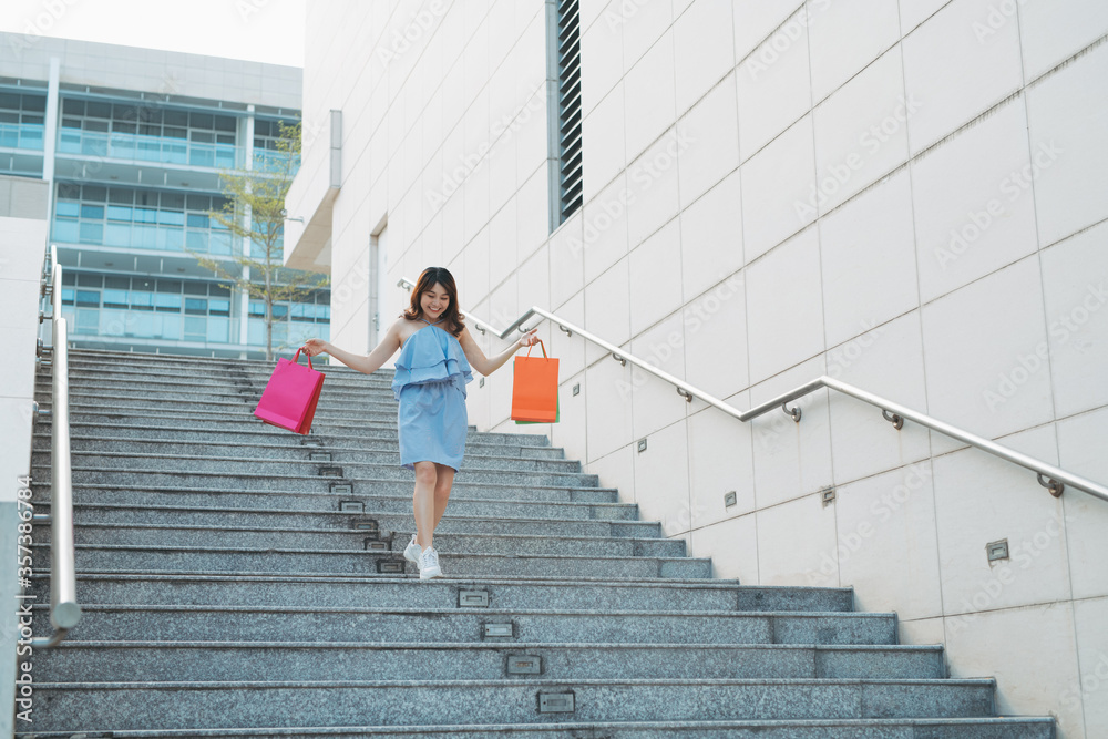 Asian young smile woman enjoy shopping with colorful bag while going down stairs.