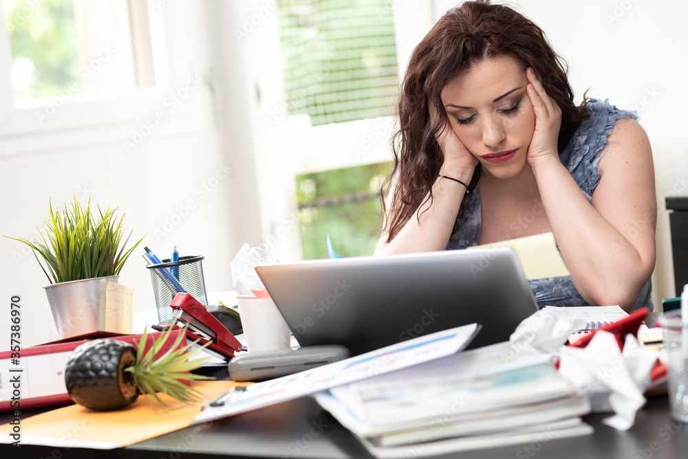 Overworked businesswoman sitting at a messy desk Overworked businesswoman sitting at a messy desk