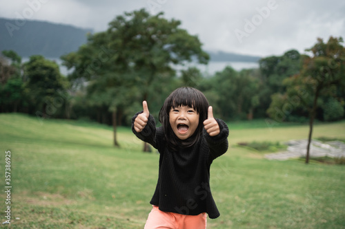 little asian girl laughing while showing thumbs up when looking at the camera