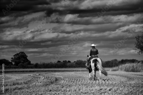 Anonymous female western horse rider. Black and white with stormy clouds, end of day 