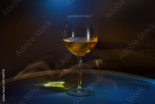 White wine in a glass on the table on a creative black background. Cigarette smoke in the bar and an alcoholic drink at a party or disco. Shooting in the dark key. Copy space