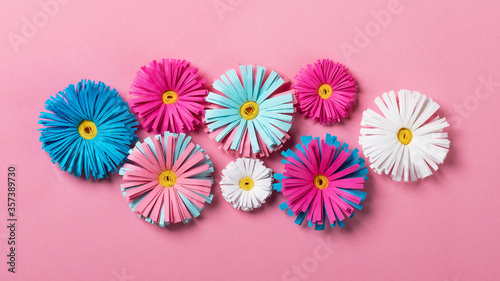 Bright colorful handmade paper flowers on pink background. Flat lay