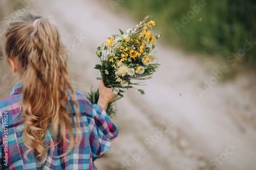 Little girl holding bouquet of wildflowers, summer evening in countryside
