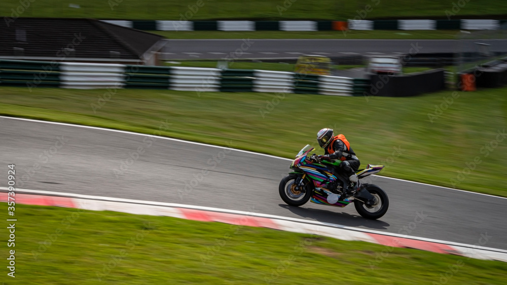 A panning shot of a multicoloured racing bike as it circuits a track