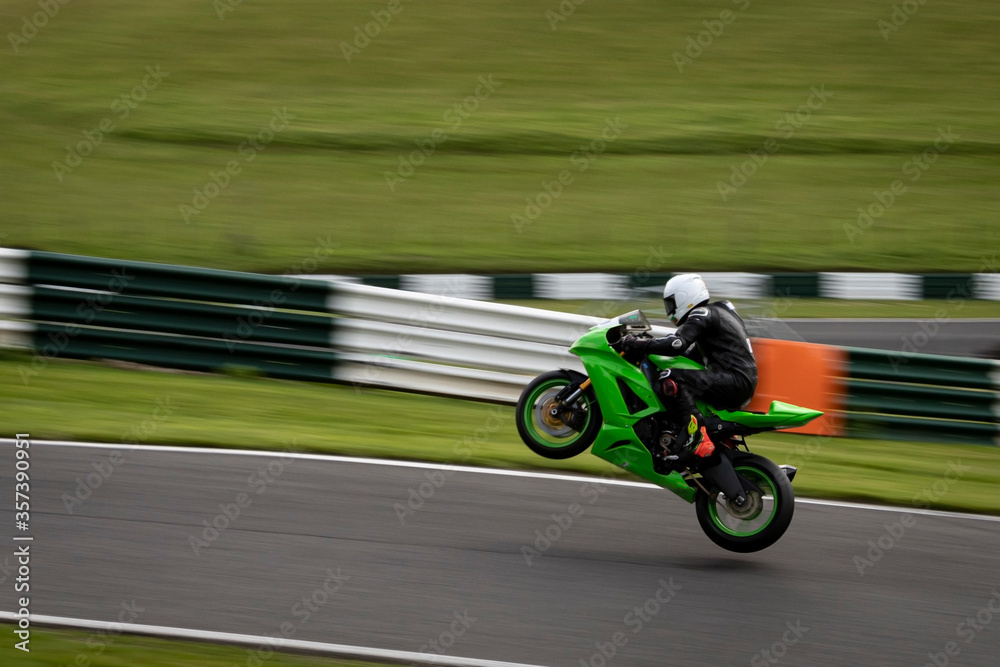 A panning shot of a green racing bike jumping off the ground altogether as it circuits a track