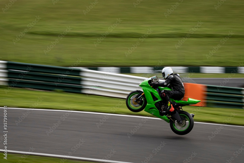 A panning shot of a green racing bike jumping off the ground altogether as it circuits a track A panning shot of a green racing bike jumping off the ground altogether as it circuits a track