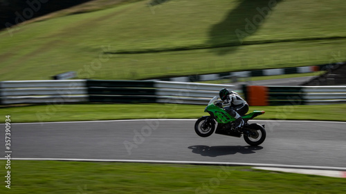 A panning shot of a green racing bike on one wheel as it circuits a track