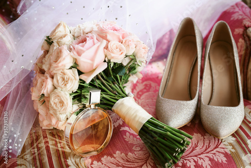 Elegant wedding accessories of an attractive bride. Wedding rings, shoes, bridal bouquet, floral arrangements, veil. Copy space for text. Background for greeting card or invitation.