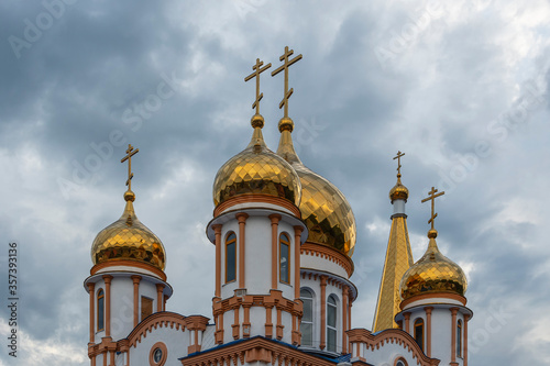 Golden domes of a snow-white Christian church against a disturbing cloudy blue summer sky