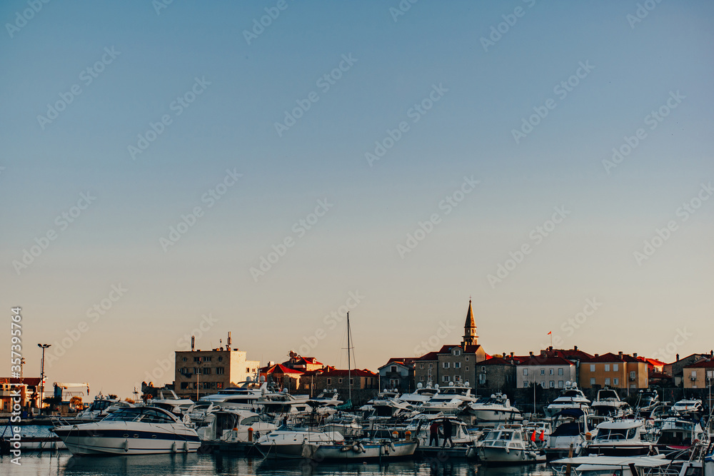 Wharf in the city of Budva, yachts moored at the walls of the old city. Sunny sunset light on rooftops.