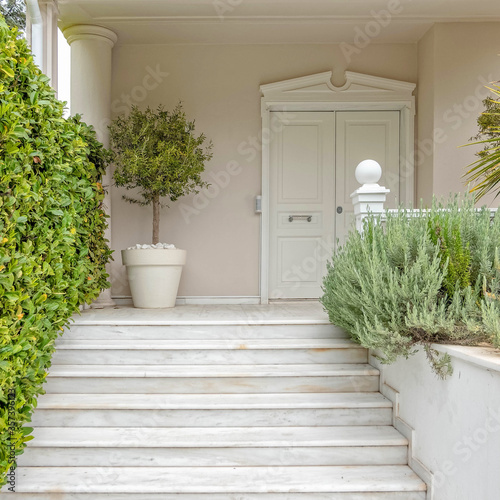 white marble stairs and door of an elegant family house entrance between vibrant green foliage