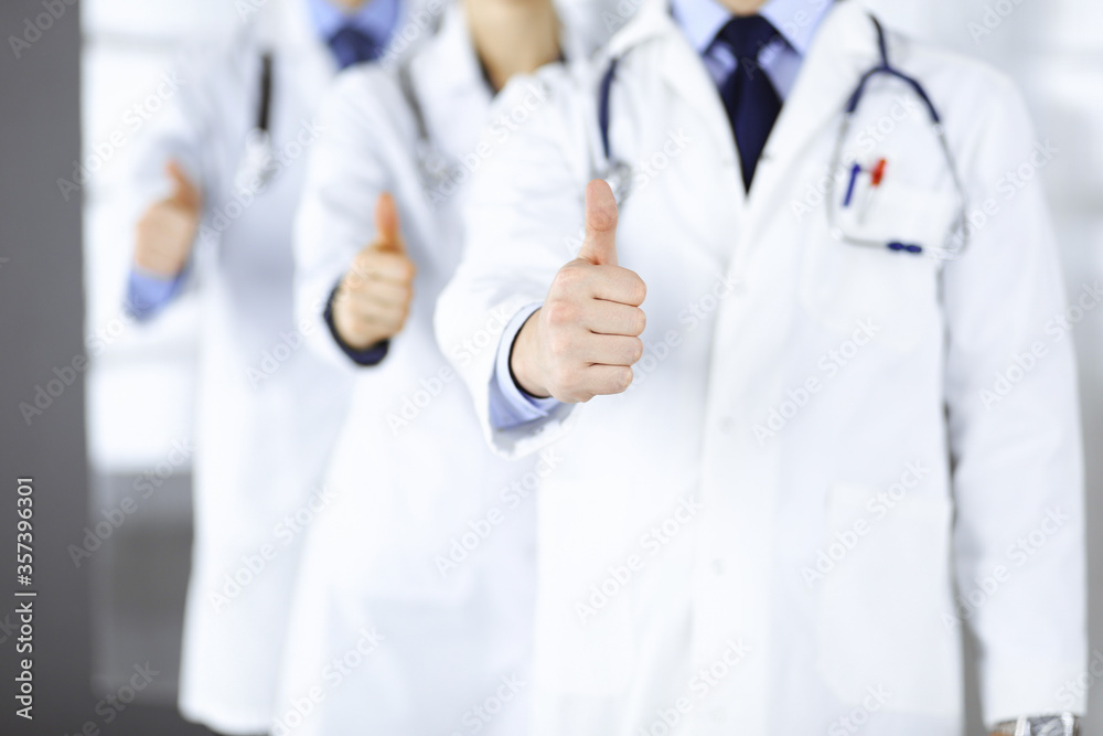 Group of unknown doctors stand as a team with thumbs up in a hospital office. Physicians ready to examine and help patients. Medical help, insurance in health care, best desease treatment and medicine Group of unknown doctors stand as a team with thumbs up in a hospital office. Physicians ready to examine and help patients. Medical help, insurance in health care, best desease treatment and medicine