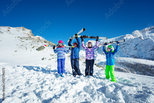Ski vacation portrait many children stand with lifting sport equipment up in the air smile, wearing color goggles and helmets