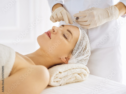 Beautiful woman receiving beauty injections with closed eyes. Beautician doctor hands doing beauty procedure to female face with syringe