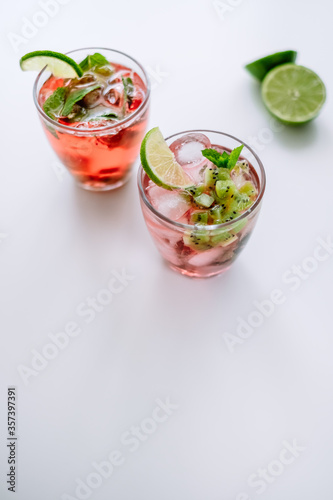Raspberry cocktail, lemonade with lime, kiwi, mint and pieces of ice on a white table.