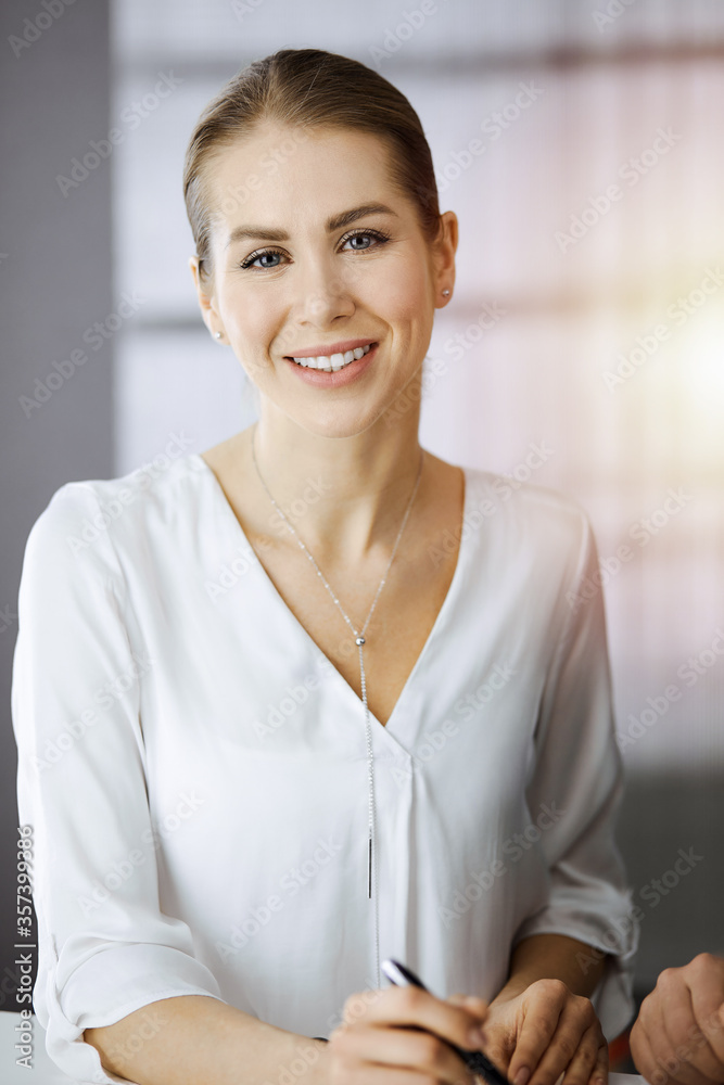 Businesswoman sitting and looking at camera in sunny office Businesswoman sitting and looking at camera in sunny office