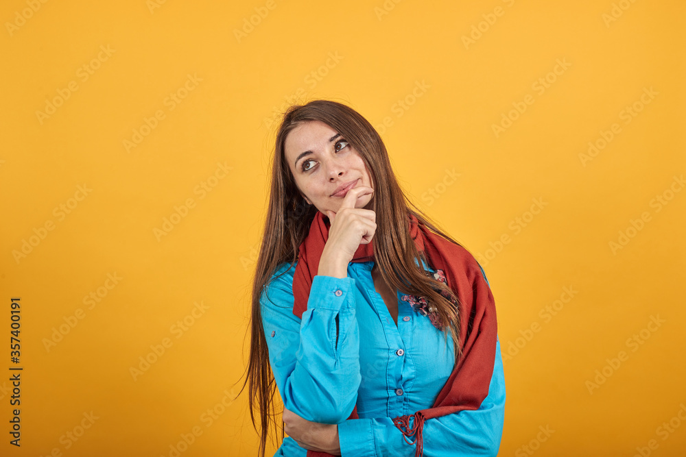 Hand on chin thinking about question, pensive expression. Doubt. Thoughtful face. Using that incredibly sharp business mind. Young attractive woman with brown hair and eyes, blue shirt, yellow Hand on chin thinking about question, pensive expression. Doubt. Thoughtful face. Using that incredibly sharp business mind. Young attractive woman with brown hair and eyes, blue shirt, yellow