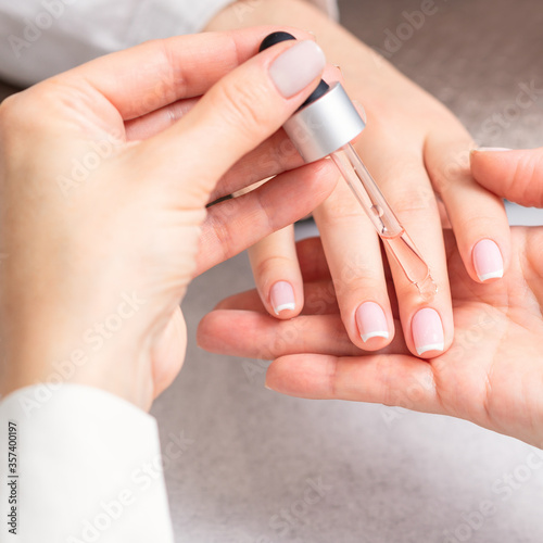 Professional manicurist pouring oil on nails french manicure of woman in beauty salon.