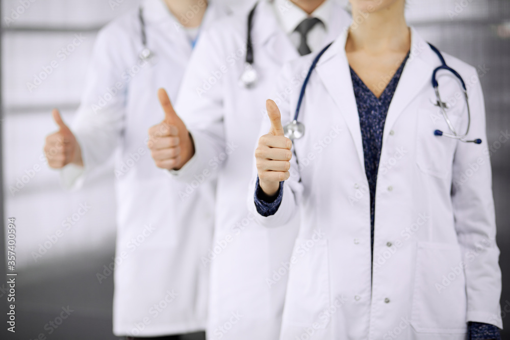 Doctors standing as a team with thumbs up in clinic and ready to help patients. Medical help, insurance and medicine concept Doctors standing as a team with thumbs up in clinic and ready to help patients. Medical help, insurance and medicine concept