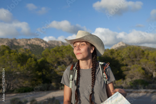 A woman hiking in the mountains of Majorca. A hiker looking at the map while traveling on the island of majorca. The girl is wearing a hat and an Australian look, has long hair and two braids.