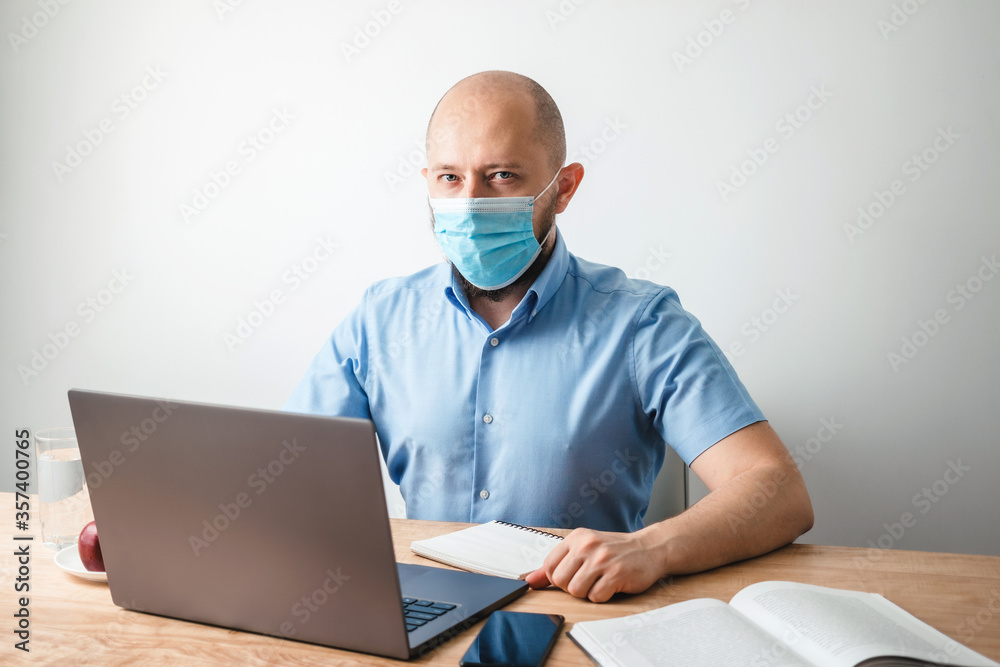Bald business man with beard wearing surgical medical mask on face as protection against coronavirus, covid-19, working or studying online on laptop at office, social isolation, quarantine concept Bald business man with beard wearing surgical medical mask on face as protection against coronavirus, covid-19, working or studying online on laptop at office, social isolation, quarantine concept