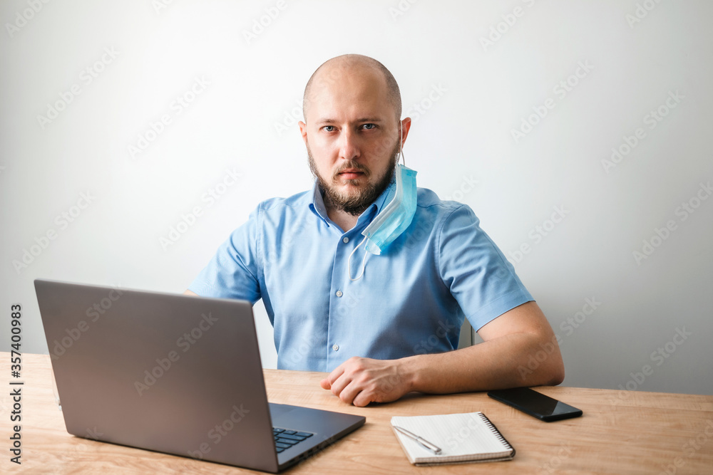 Bald business man with beard takes off surgical medical mask on face as protection against coronavirus, covid-19, working or studying online on laptop at office, social isolation, quarantine concept Bald business man with beard takes off surgical medical mask on face as protection against coronavirus, covid-19, working or studying online on laptop at office, social isolation, quarantine concept