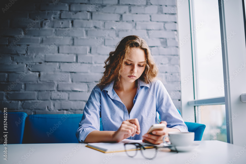 Emotional hipster girl rejoicing sms message on cellular sitting at book Emotional hipster girl rejoicing sms message on cellular sitting at book