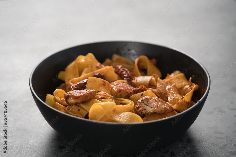 fettuccine pasta with fried chicken and sun-dried tomatoes in black bowl on concrete background fettuccine pasta with fried chicken and sun-dried tomatoes in black bowl on concrete background