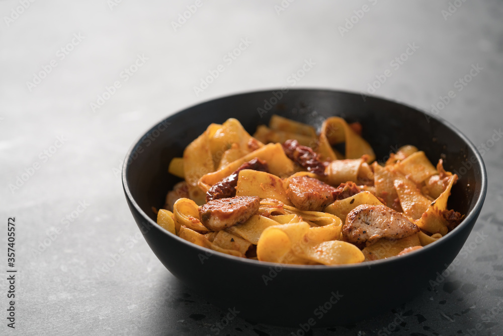 fettuccine pasta with fried chicken and sun-dried tomatoes in black bowl on concrete background fettuccine pasta with fried chicken and sun-dried tomatoes in black bowl on concrete background