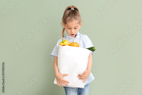 Surprised little girl with food in bag on color background
