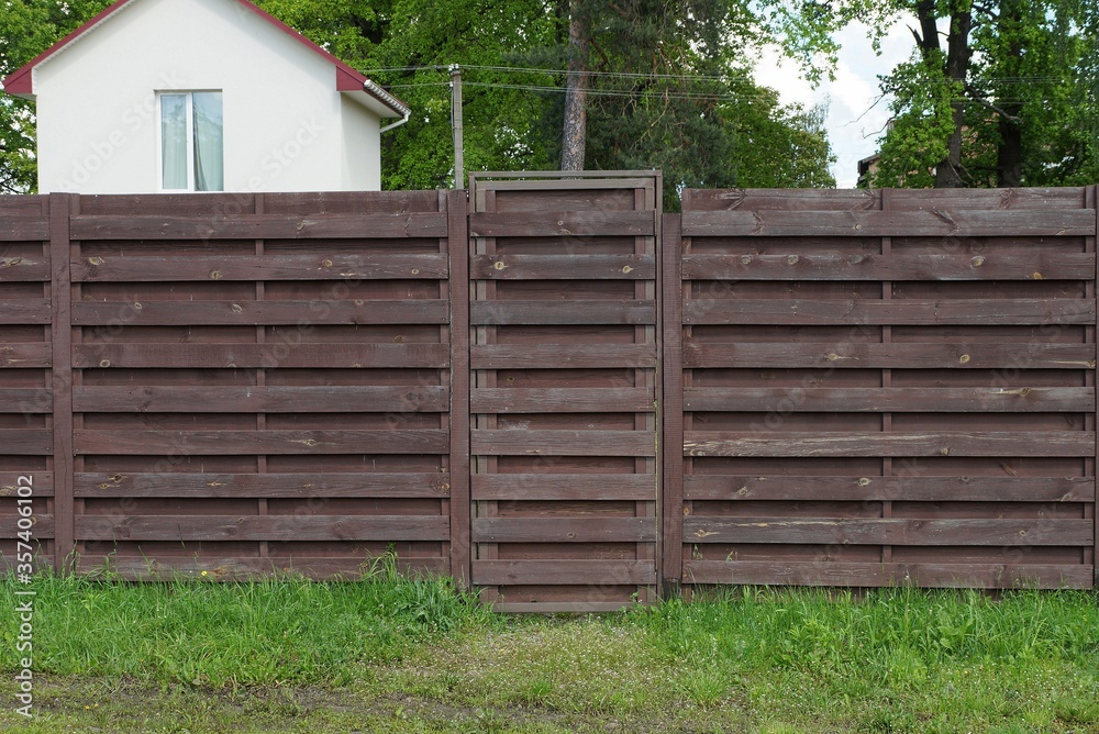 brown wooden fence wall and closed door on the street in green grass brown wooden fence wall and closed door on the street in green grass