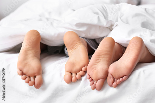 Legs of young couple lying under blanket in bed