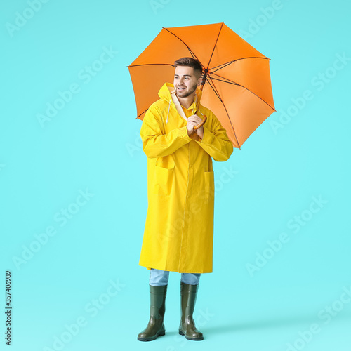 Young man in raincoat and with umbrella on color background photo