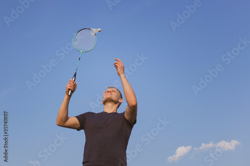 Young Caucasian man plays badminton on a background of blue sky. The concept of an amateur game of badminton, outdoor activities. Copyspace, bottom view.
