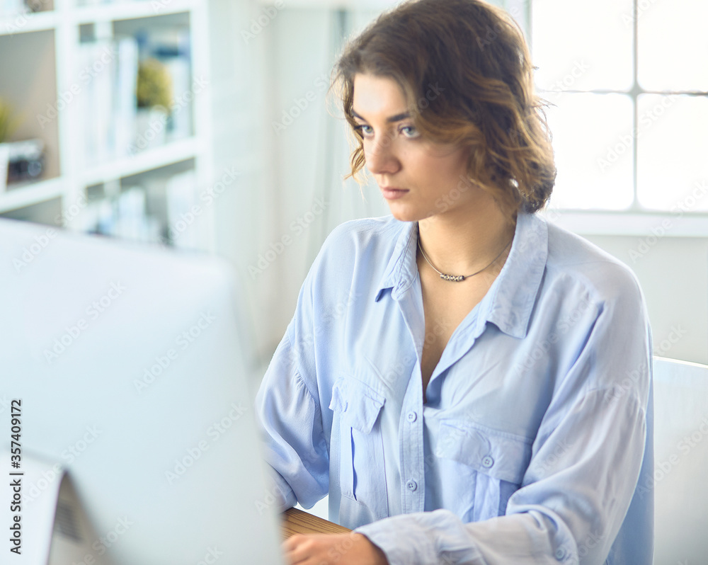 Pretty young woman sitting at desk and typing on laptop Pretty young woman sitting at desk and typing on laptop