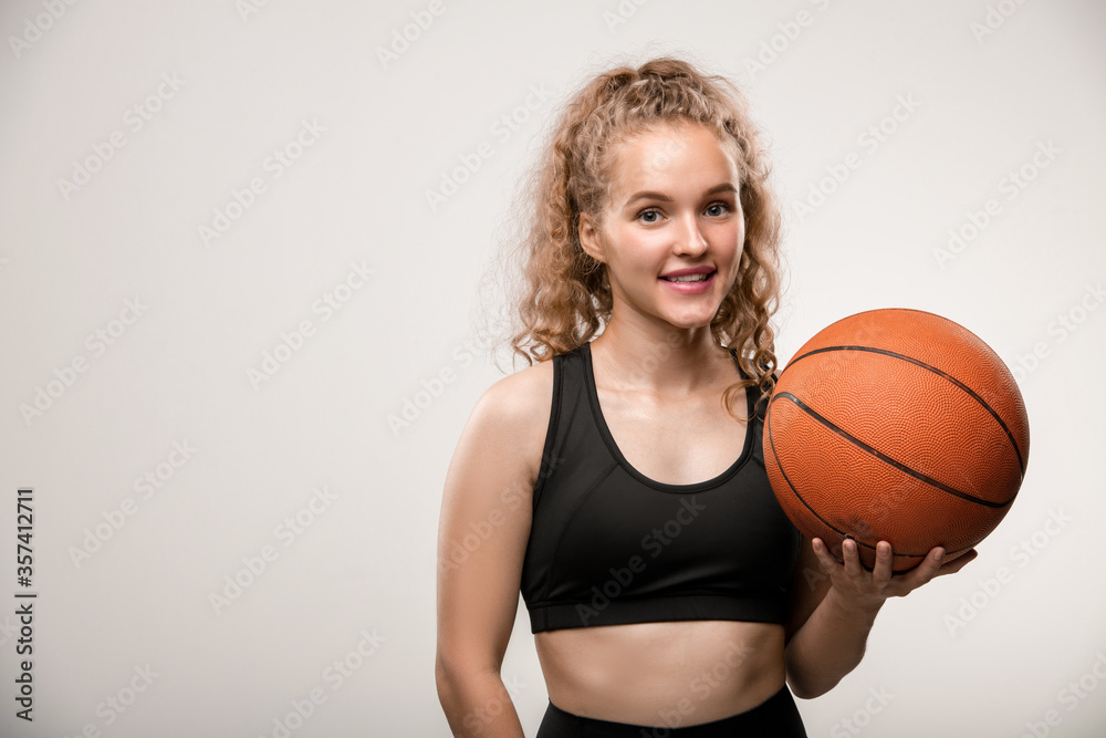 Happy young successful female basketball player in black tracksuit holding ball