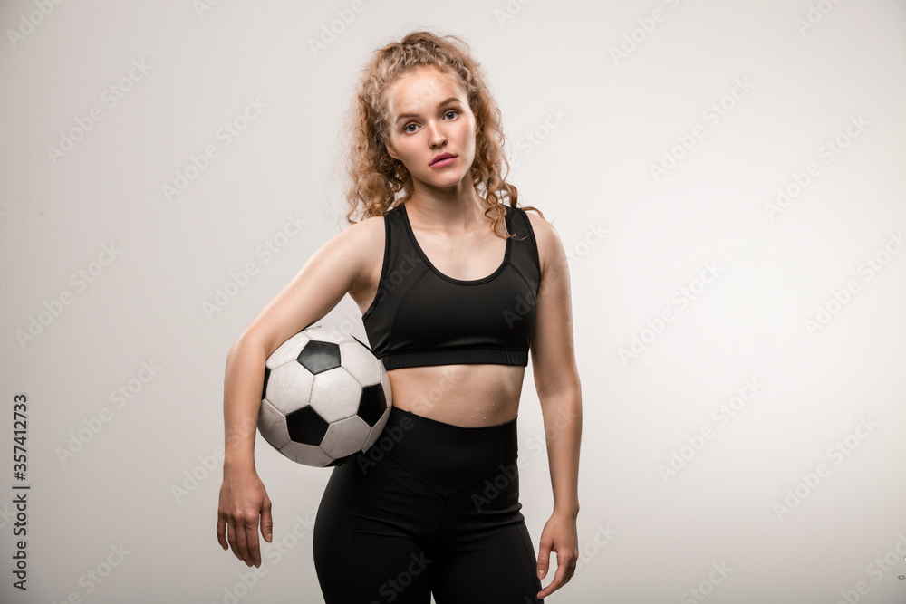 Pretty young female soccer player with long blond curly hair holding ball
