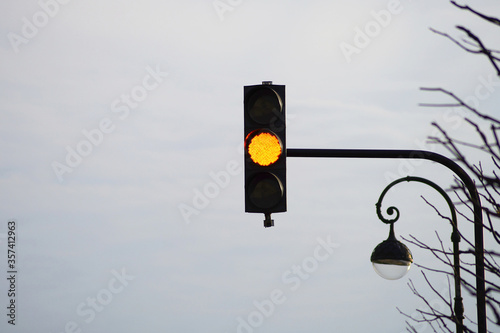 Pedestrian traffic light with yellow signal. Yellow traffic light on sky background. Traffic light and street lamp.