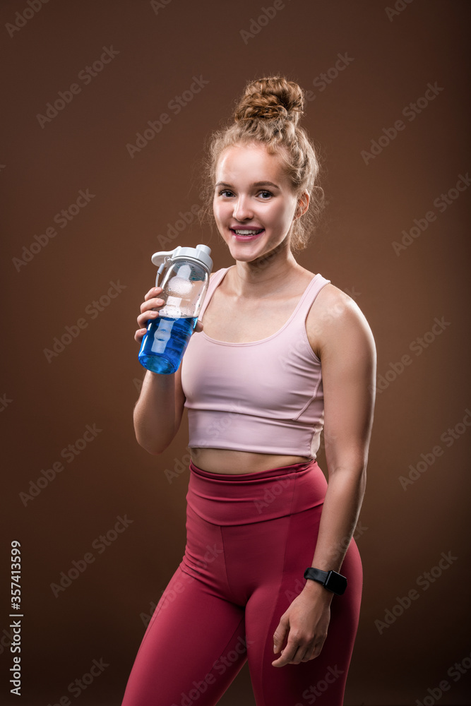 Fit cheerful sportswoman with toothy smile holding bottle with refreshing drink Fit cheerful sportswoman with toothy smile holding bottle with refreshing drink