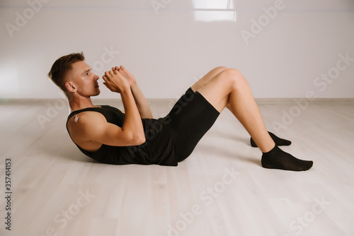 Young man in sportswear doing press exercise on fitness mat at home