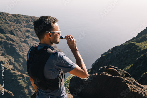 Portrait of young man drinking energy sports nutrition energy gel while sitting and resting after trail running